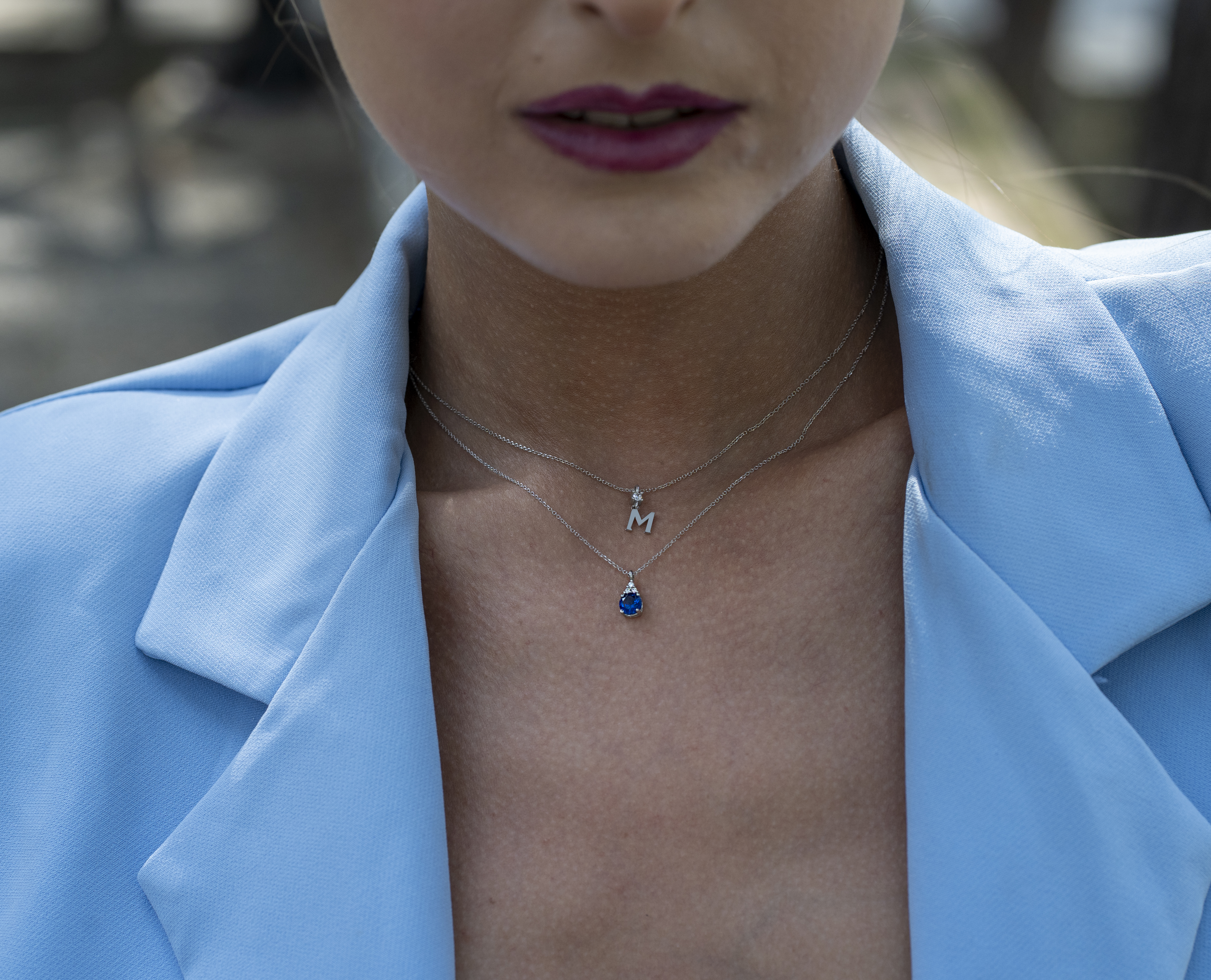 K9 white gold necklace with a teardrop-shaped pendant adorned with a round blue stone.